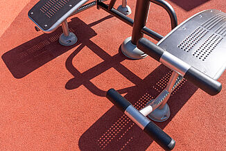 Gros plan sur le revêtement de sécurité et sportif REGUPOL sans joints, absorbant les chocs, installé sous des équipements de fitness en plein air dans une aire de jeux et de loisirs accessible à tous, située à Berlin-Steglitz-Zehlendorf.