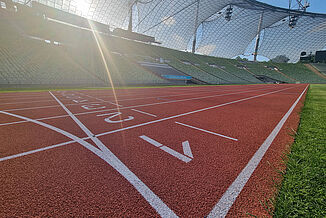 Ligne d’arrivée de la piste au stade olympique de Munich sous le soleil. Vue en contre-plongée de la piste rouge au stade olympique de Munich sous le soleil. La ligne d’arrivée avec marquages de couloirs est clairement visible au premier plan.