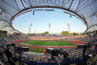 Stade olympique de Munich pendant l’Euro d’athlétisme 2022 – piste rouge, caméras et ambiance internationale. Vue intérieure du stade olympique de Munich lors des Championnats d’Europe d’athlétisme 2022. La piste rouge et le terrain central sont prêts pour la compétition, avec caméras et spectateurs créant une ambiance en direct.