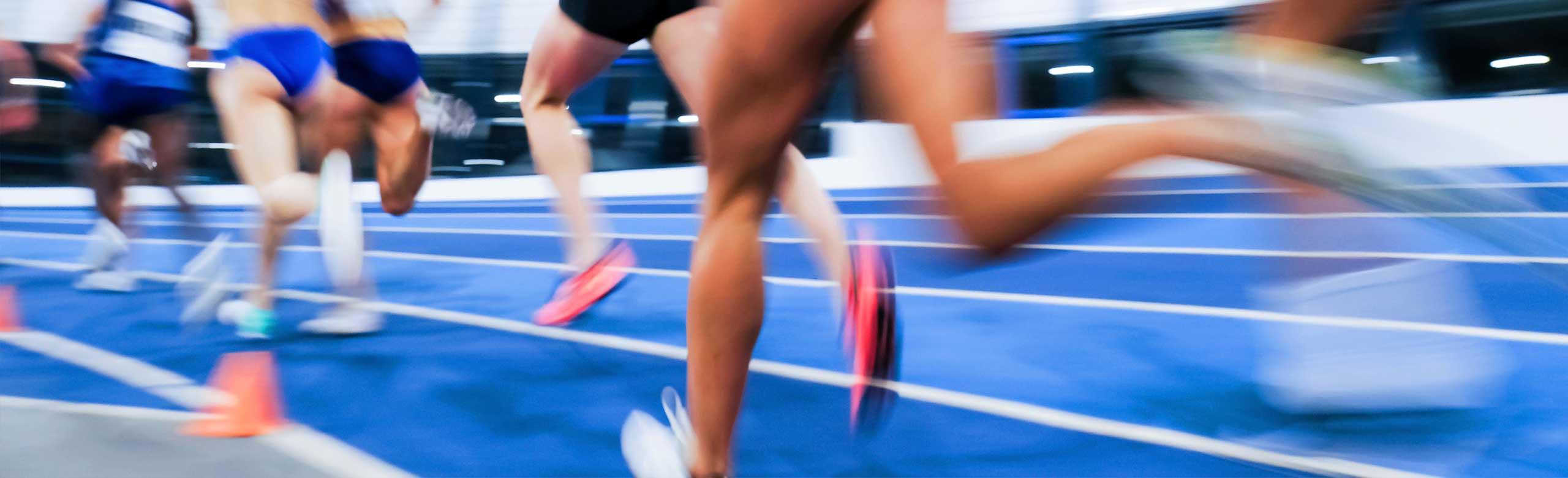 Athlètes féminines sprintant lors d'une compétition d’athlétisme. Image dynamique d'une course d’athlétisme, coureuses sprintant sur une piste bleue, flou de mouvement soulignant la vitesse et l’intensité de la compétition.