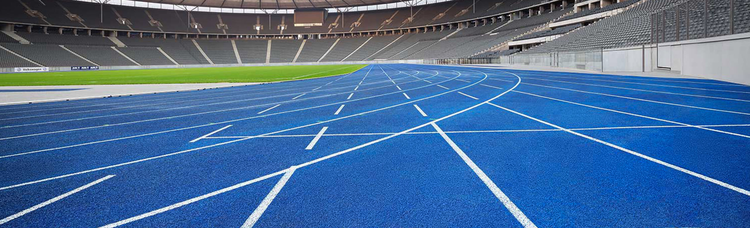 Empty blue running track at Berlin Olympic Stadium – the Blue Miracle. Curved track lanes with white markings in front of empty stands. The blue synthetic running track at Berlin Olympic Stadium, known as “the Blue Miracle.” Curved lanes in front of empty stands represent a modern athletics surface in a world-class track and field venue.