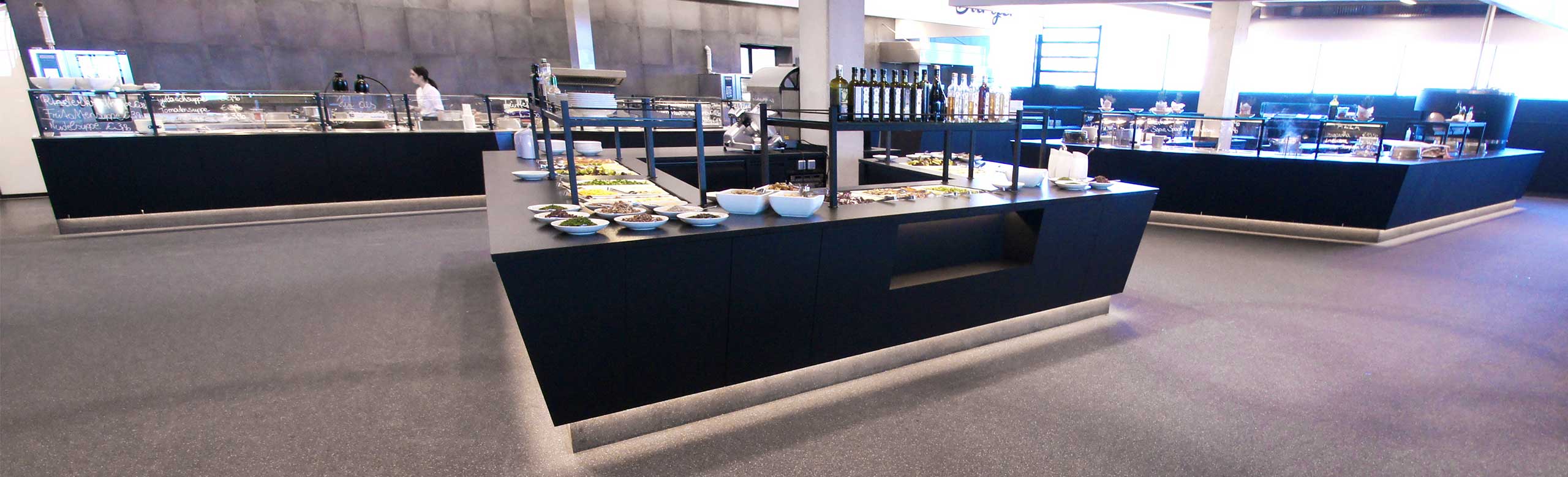 Un espace de restauration dans une station de remontées mécaniques. Un espace de restauration dans une station de remontées mécaniques. L'espace est recouvert d'un revêtement de sol clair, un grand buffet moderne de couleur noire se trouve au centre.