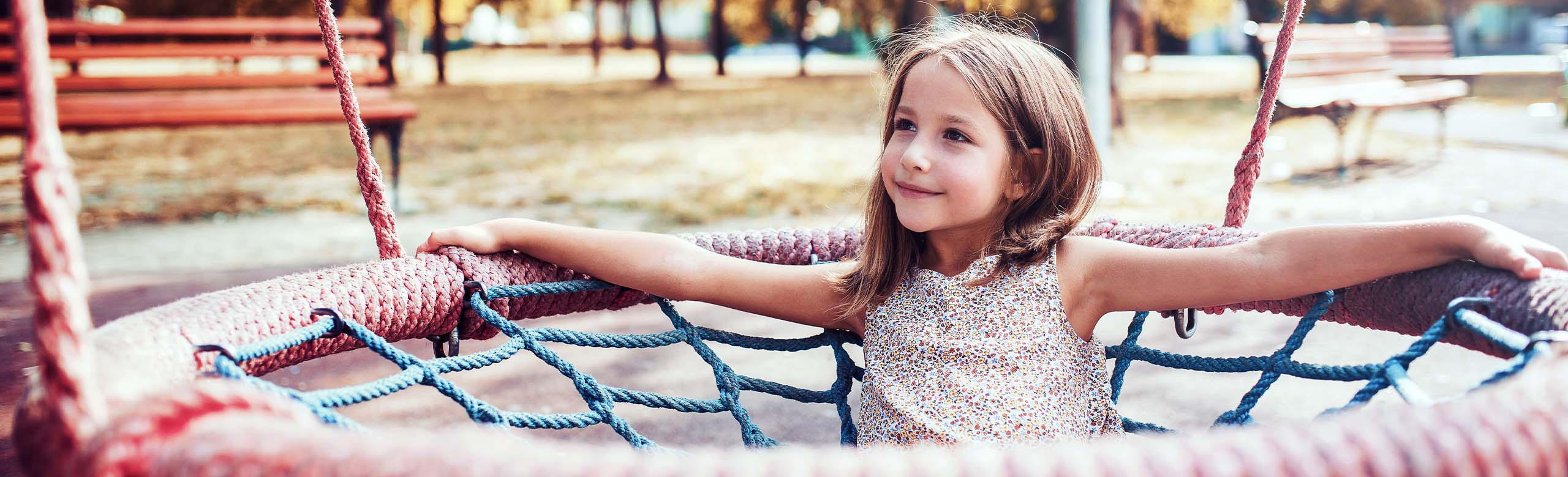 Child on a playground with REGUPOL playfix block step - the elastic block step for edging play areas. Smiling child in a nest swing on a playground with REGUPOL playfix block step - elastic block step for edging play and sports areas